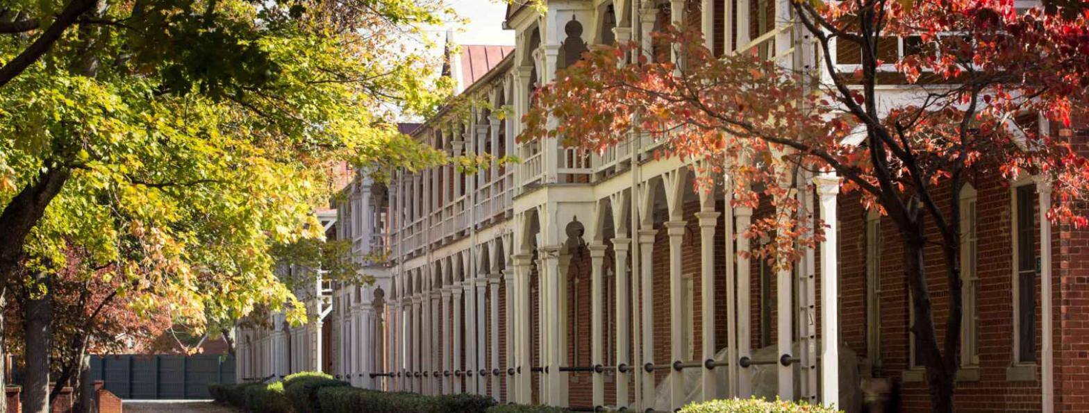 A long arcaded row of historic red-brick buildings with white timber colonnades and balconies, under autumn trees.